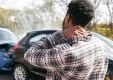 Young man in pain, whiplash neck injury, by damaged car after accident.